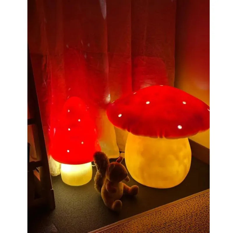 Two small handcrafted red mushroom lamps with glowing caps and yellow stems light up a children's room decor. A plush squirrel toy sits between the Lamp Small Mushroom Red on the floor, framed by sheer curtains illuminated by their glow.