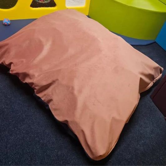 A Sensory Crash Bag Large in brown rests on a dark carpet in a vibrant room with green, yellow, and blue walls. A small ball sits nearby, emphasizing the therapeutic benefits of this calming environment.