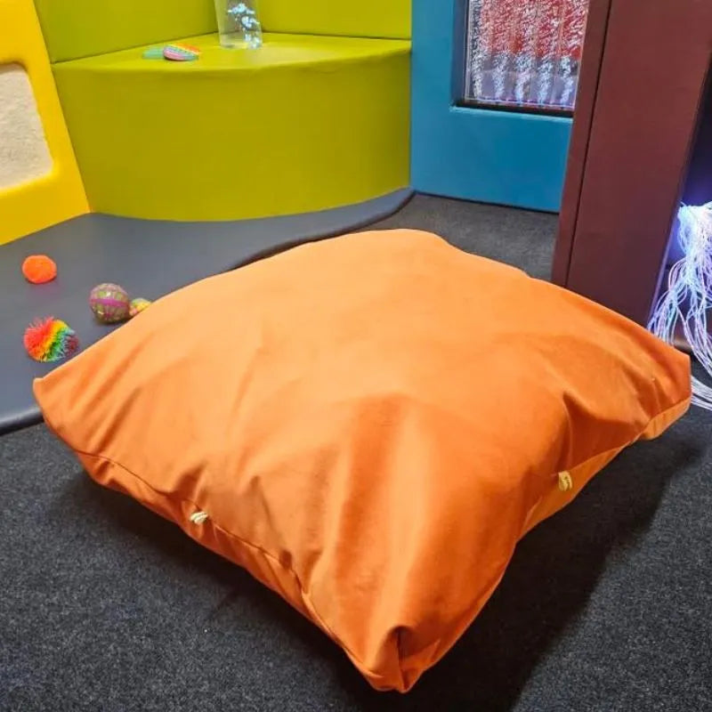 A small orange Sensory Crash Bag sits on a dark carpet in a colorful room with sensory toys, including textured balls, providing therapeutic benefits for emotional regulation in children.