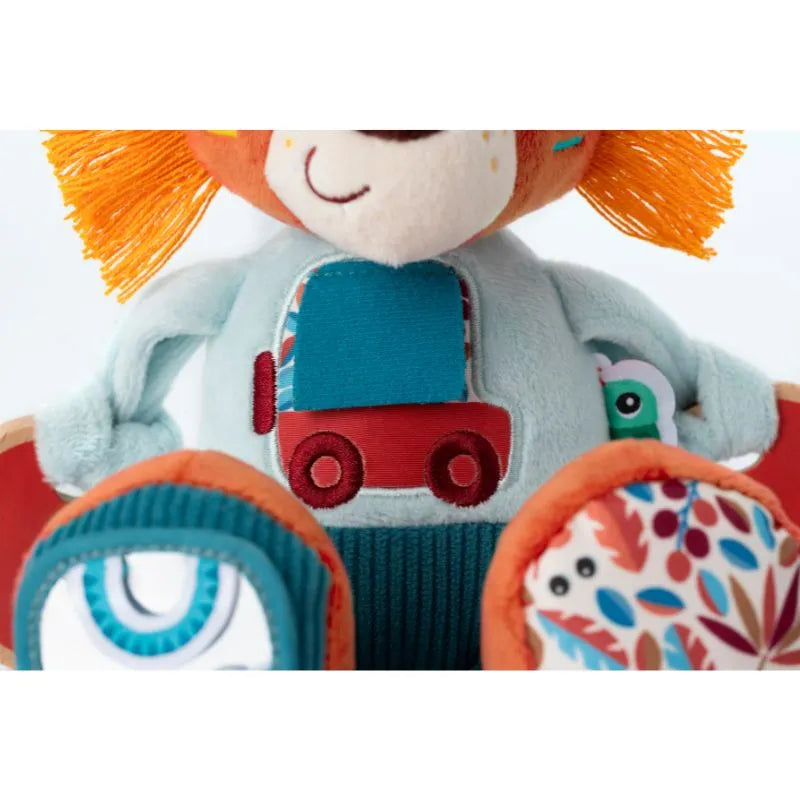 Close-up of the Lilliputiens I'm Discovering Jack Multi-Activity Lion, a sensory soft toy with orange hair and a blue shirt with a red and blue truck. The arms and legs feature colorful, patterned fabric with floral designs and abstract shapes to spark curiosity in babies.