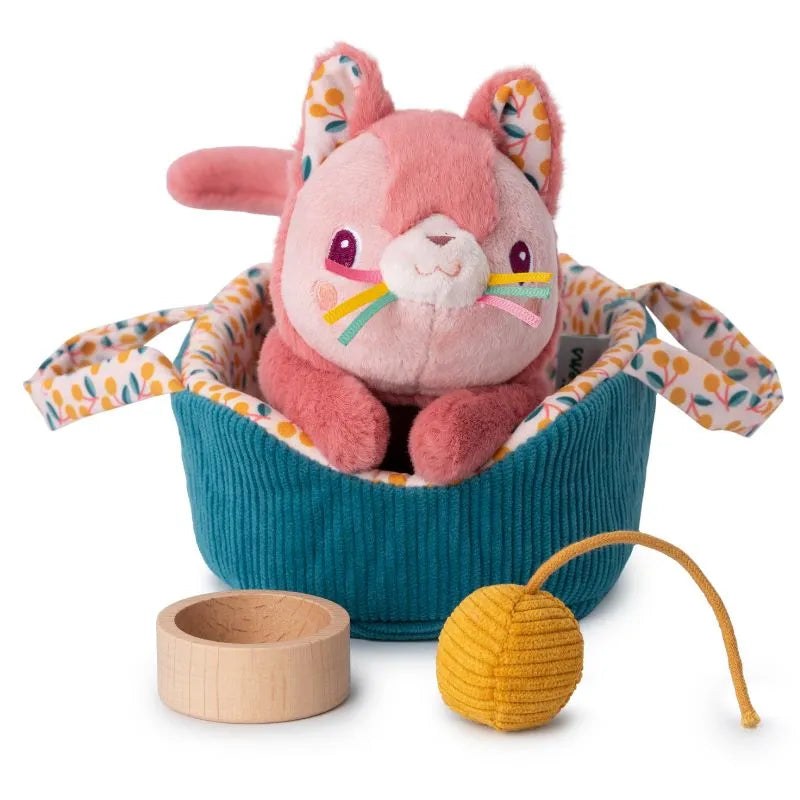 The Lilliputiens I'm Exploring Jeanne Cat With Basket features a plush pink cat toy with rainbow whiskers, nestled in a teal floral-handled basket. It includes a small wooden bowl and textured yellow ball on a string, perfect for nurturing caring skills as a children's toy.