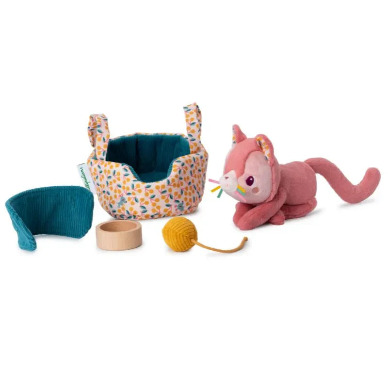The Lilliputiens I'm Exploring Jeanne Cat With Basket features a plush pink kitten with a yellow yarn ball, a small wooden bowl, and a floral patterned fabric basket, along with a cozy blue fabric piece beside the basket.