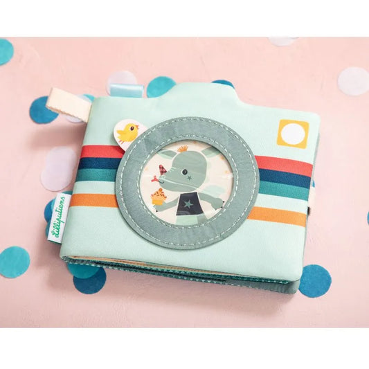 The Lilliputiens I'm Discovering Joe Photo Album makes an ideal gift for parents, featuring a soft fabric design resembling a camera with a circular window displaying a cartoon alien and chick. Its light blue color with colorful stripes on a pink confetti-dotted surface creates an adorable keepsake.