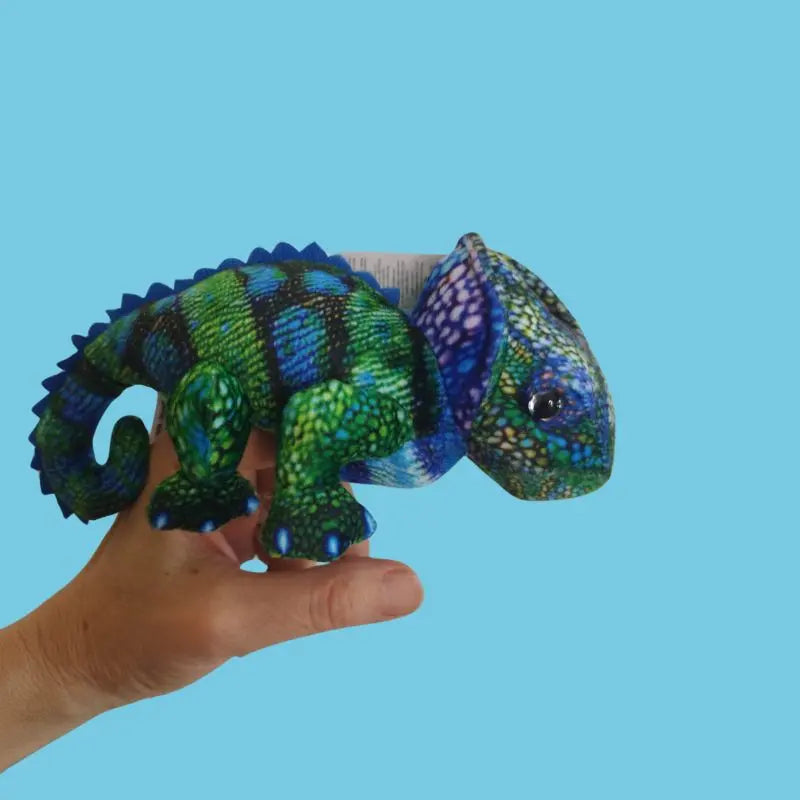 A hand holds The Puppet Company Chameleon (Blue-Green) Finger Puppet from the Little Creatures Range against a plain light blue background.