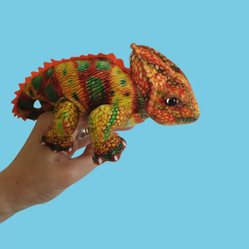A hand holds The Puppet Company Orange Chameleon Finger Puppet from the Little Creatures Range, displaying its soft, realistic yellow, green, red, and orange patterns against a plain light blue background—perfect for colourful adventures.