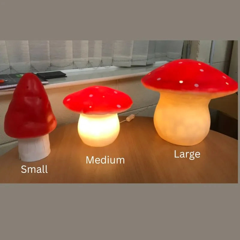 The Lamp Large Mushroom Red is a glowing, handcrafted lamp from Germany featuring a red cap with white spots, perfect as a charming decorative children's lamp. It's displayed alongside small and medium versions on a table.