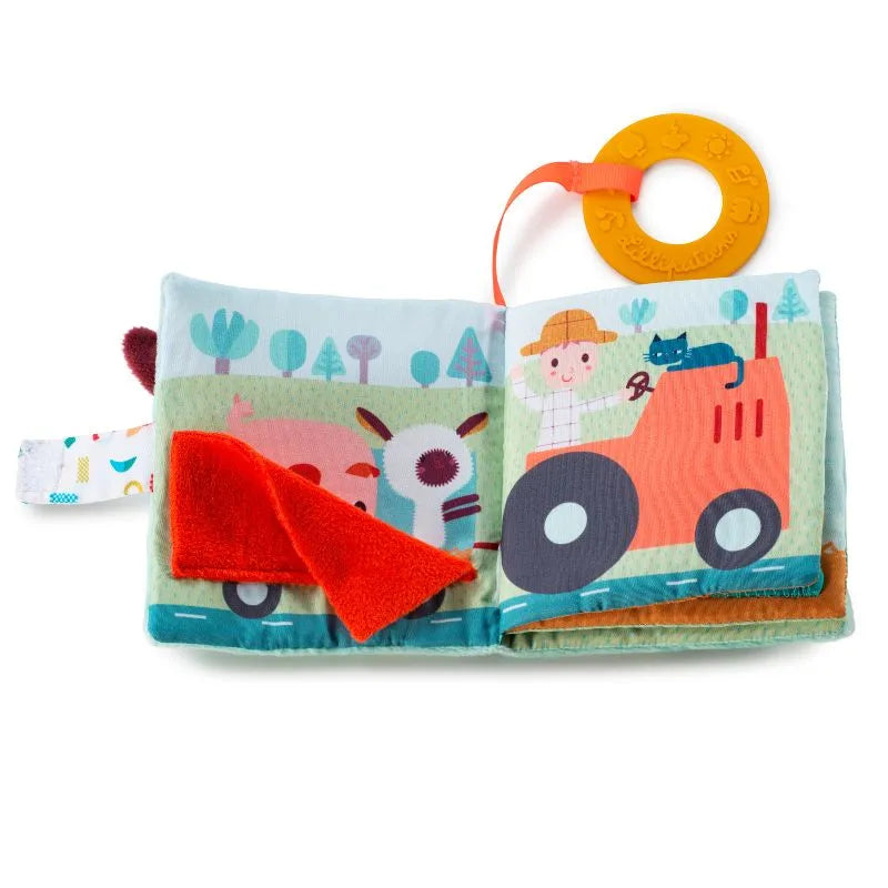 The Lilliputiens I'm Discovering Playbook Farm is a soft, farm-themed book with colorful illustrations and crinkly pages. It shows a pig with a red flap on the left and a farmer in a red tractor with a cat on the right. An attached yellow teething ring adds extra fun.