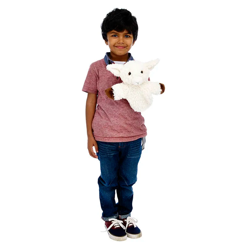 A young child with dark hair, in a red shirt and blue jeans, stands smiling while holding The Puppet Company CarPets White Sheep hand puppet against a plain white background.