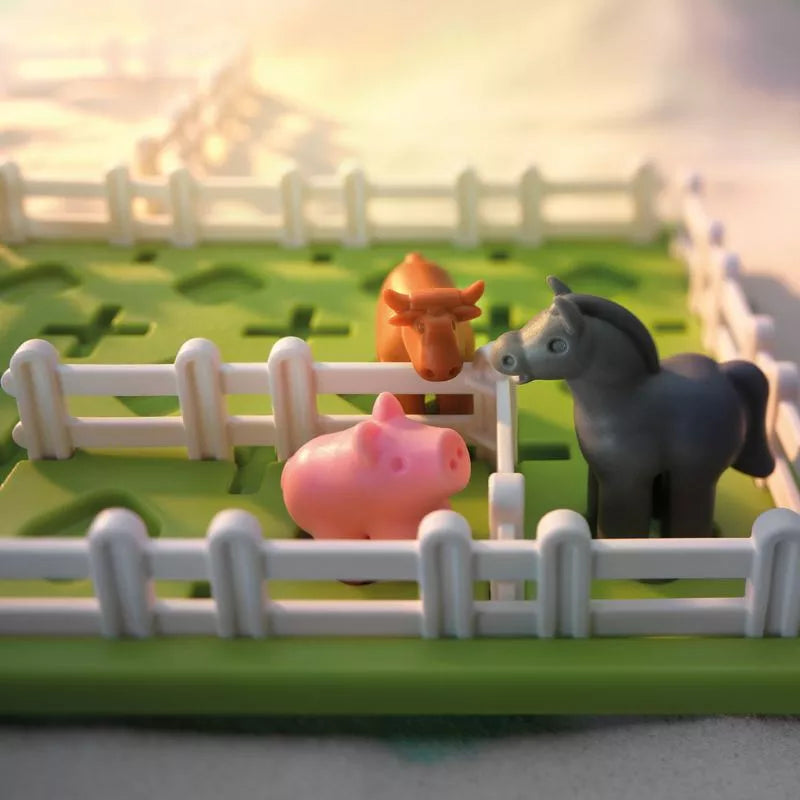 The SmartGames Smart Farmer set features a small fenced area on a green board with toy farm animals—a cow, pig, and horse—offering vibrant play scenes and problem-solving adventures for transformative and engaging fun.
