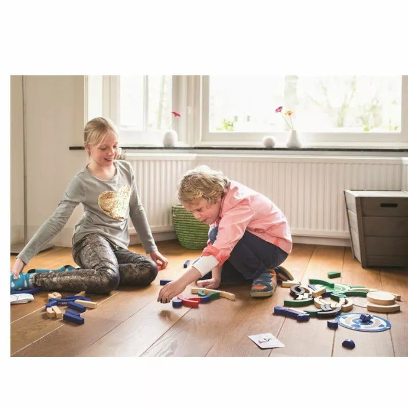 Two kids sit on a wooden floor, playing with the colorful Buitenspeel Sport Blocks Puzzle Game. Bright natural light streams through the window, creating an engaging atmosphere as they immerse themselves happily in imaginative play.
