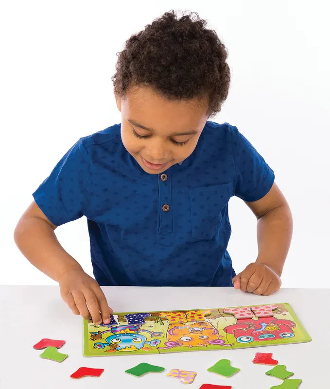 A child in a blue shirt is playing with the Orchard Toys Smelly Wellies puzzle on a white table, which features cartoon animal characters and various shapes scattered around. The child is focused on assembling the pieces.