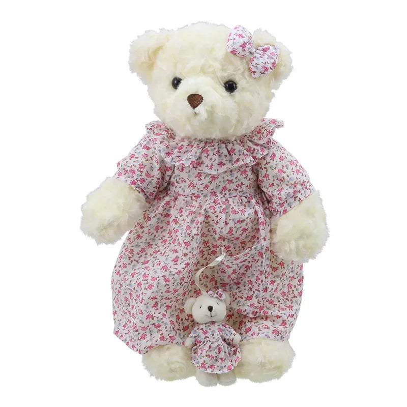 A Wilberry Dressed Animal Bedtime Bear Nightie dressed in a floral, pink and white dress, with a matching bow on its head. It is holding a smaller baby bear also dressed in a coordinated floral outfit. Both teddy bears are looking forward with a cute and cuddly appearance. Ideal as a charming birthday present!