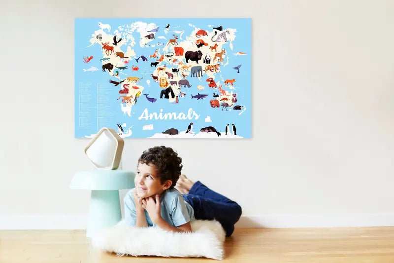 A young child smiles on a fluffy white rug with the Poppik Discovery Sticker Poster – Animals of the World, a blue illustrated map featuring endangered animals, displayed on the wall behind them.