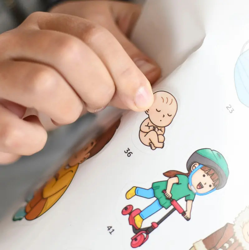 A hand peels an educational baby sticker from the Poppik Discovery Sticker Poster – Human Body sheet, with other stickers like a child on a scooter and numbers, ideal for use with the interactive human body poster.
