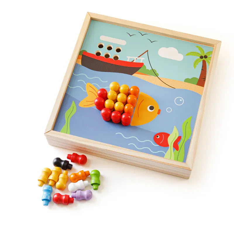 The Bigjigs Seaside Peg Board is a wooden puzzle toy that enhances fine-motor skills and features a fish with colorful red, yellow, and orange pegs. The sea-themed background includes a boat, palm trees, and birds. Colorful pegs invite interactive play scattered beside the board.