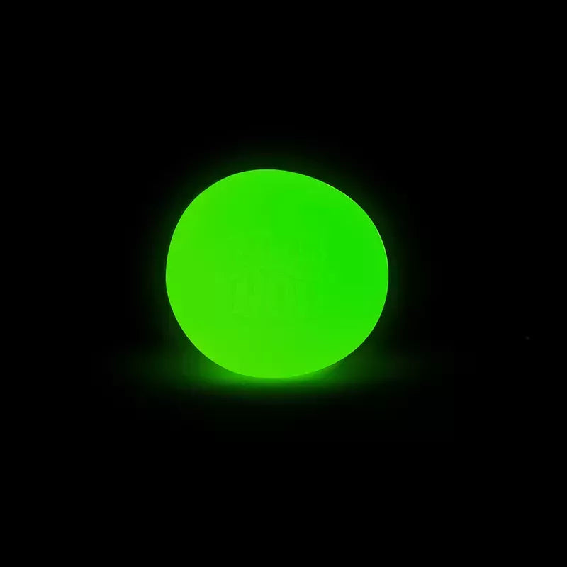 A bright neon green Glow in the Dark Needoh glowing intensely against a pitch-black background.