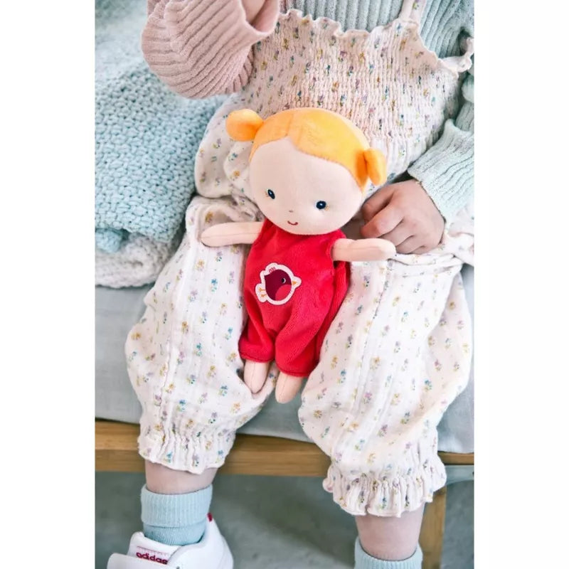 A little girl sitting on a bed holding Lilliputiens Agathe Baby First Doll.