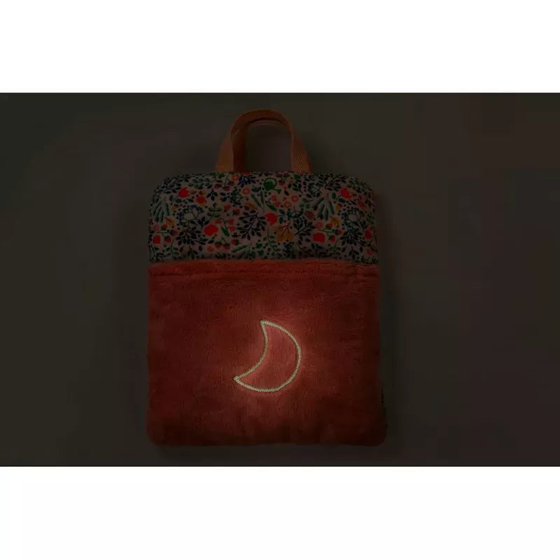 A dimly lit image showcasing a Lilliputiens Stella Bed Time Ritual with a colorful floral pattern at the top and a crescent moon design glowing on its lower suede-like textured section, perfect for children's bedtime adventures.