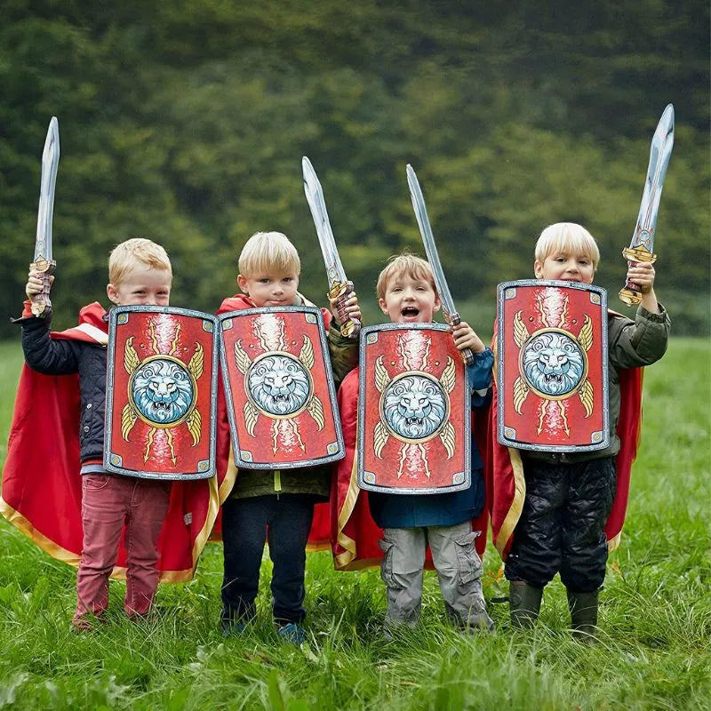 Four kids in Liontouch Roman Capes engage in a puppet show with shields in a field.