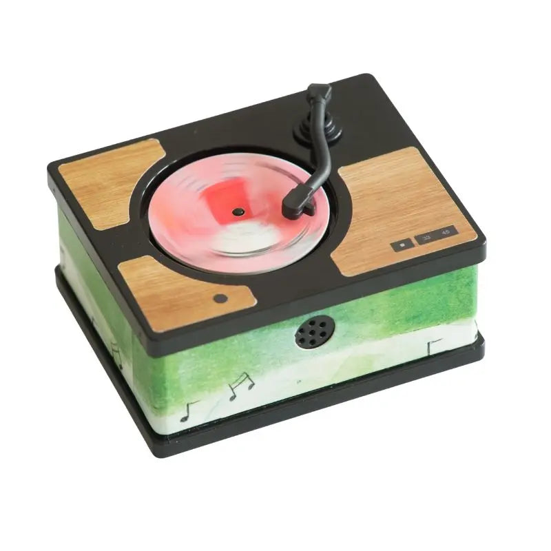 The Mini Gramophone Box Set is a miniature toy turntable with a red and white vinyl record, black tonearm, wood-patterned accents, and a green base with musical notes—perfect for playing traditional Irish songs—plus a front speaker grille.