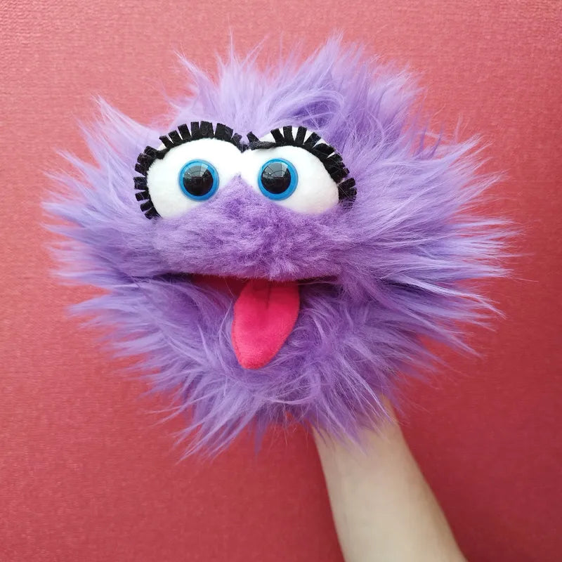 The Living Puppets Flob Hand Puppet, resembling a fluffy purple monster with large blue and white googly eyes, black eyelashes, and a pink tongue sticking out, is perfect for creative play. With its mischievous expression set against a pinkish-red background, it adds charm and fun to any imaginative activity.