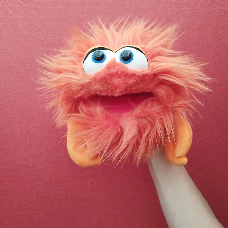 A beige hand holds the Living Puppets Monster Hand Puppet Knipser, a bright orange, furry monster puppet with large, round white eyes and a wide-open mouth. The mouth-moving hand puppet appears to be smiling against a solid, textured red background.