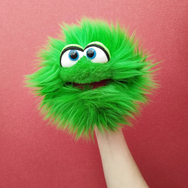 A green, fuzzy Living Puppets Blappermouth Hand Puppet with large blue eyes and a wide, red mouth is held up against a red background. The creation looks like a friendly monster with a cheerful expression, perfect for creative play.