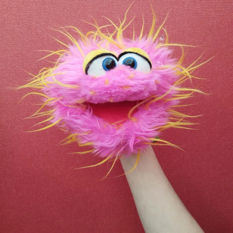 A vibrant and playful Living Puppets Monster Hand Puppet Knaller, featuring large round eyes, a wide open movable mouth, and fur adorned with pink and yellow accents, is being held against a red background.