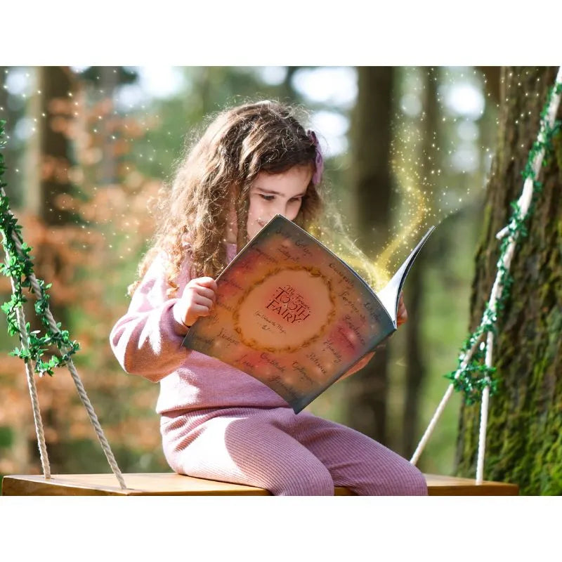 A young girl sits on a wooden swing outdoors, reading a magical book as sparkles float from its pages. Next to her is the My Forever Tooth Fairy Gift Set, adding to the enchanting scene beneath the trees as she becomes lost in her story.