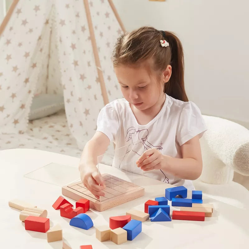 A young child with brown hair enhances her spatial awareness by playing with the 3D Block Building Game on a table. As she places pieces on a grid board, it becomes both fun and a problem-solving activity. A star-patterned play tent is visible in the background.