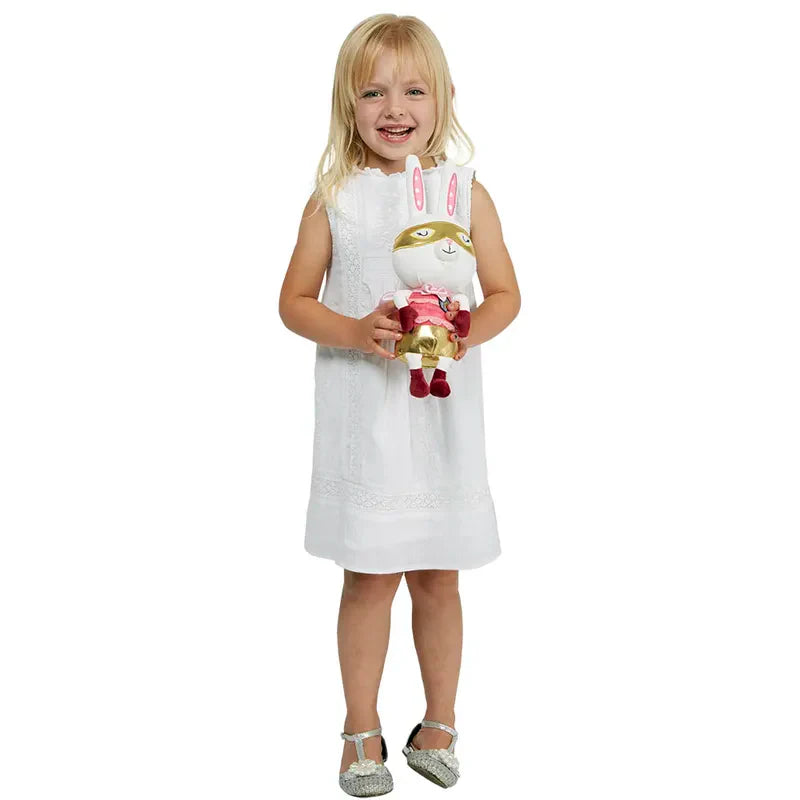 A young girl with blonde hair, wearing a white dress, smiles while holding a Wilberry Super Hero Rabbit dressed in a colorful outfit with a mask. The imaginative play comes to life as she stands against a plain white background.