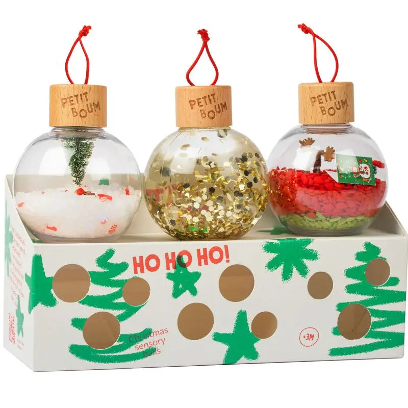 Christmas Sensory Baubles—set of three clear, unbreakable baubles handmade in Spain with wooden lids and red loops, filled with festive white, gold, and red materials. Presented in a “HO HO HO!” box with green tree decor—ideal for holiday display.