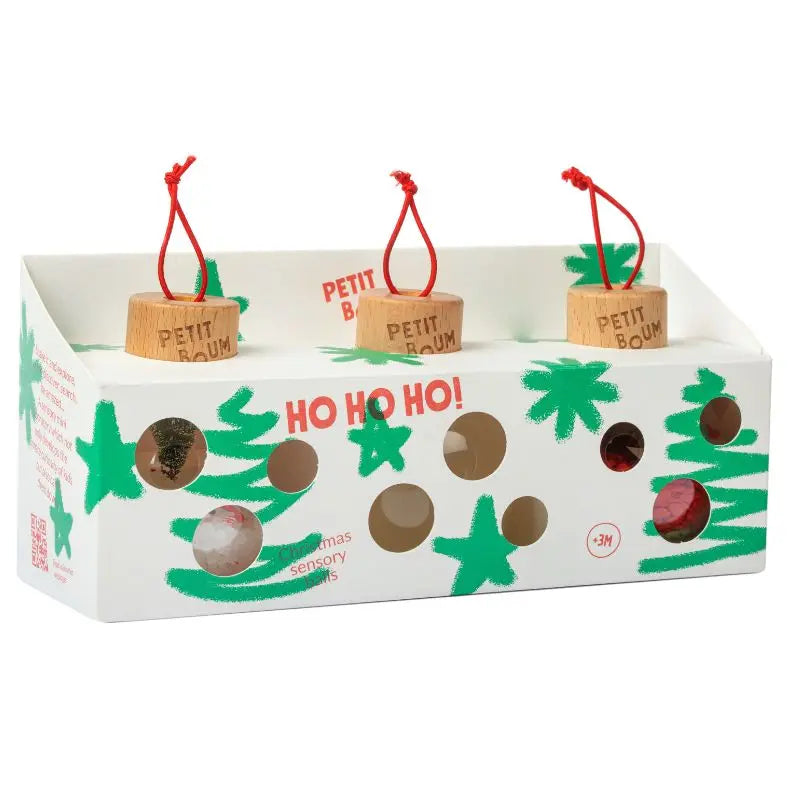 A white "HO HO HO!" box with green star and tree designs holds three handmade Christmas Sensory Baubles by PETIT BAUM, each wooden ornament from Spain featuring red loops, engraved branding, and festive red and silver details inside.