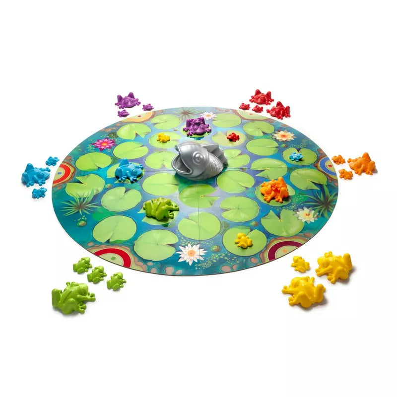 SmartGames Froggit, a colorful board game with a circular lily pad design and a central silver frog, promotes flexible thinking. Multicolored plastic frogs in green, blue, red, yellow, purple, and orange represent a vibrant frog family around the board.