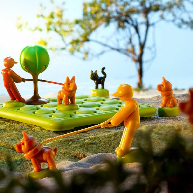 A whimsical diorama featuring colorful toy figures and dogs on leashes, set against a backdrop with a tree and a cat, is reminiscent of the SmartGames Walk The Dog game. This playful scene rests on a grid-like platform, transforming it into an engaging miniature park adventure.