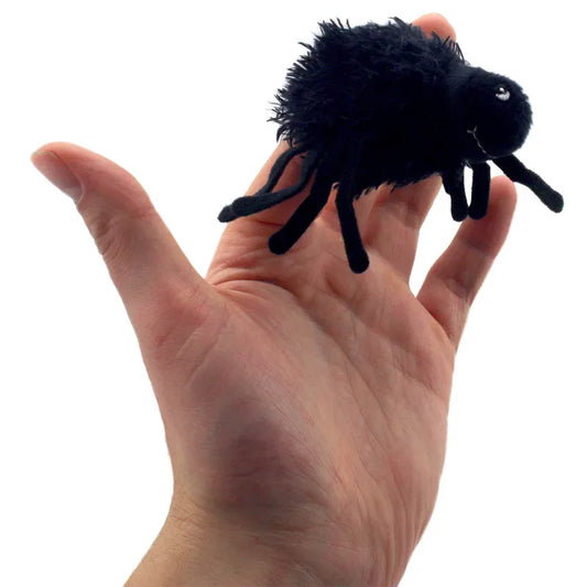 A hand showcases "The Puppet Company Finger Puppet Spider Furry," a small, plush black spider with multiple legs and two white eyes, reminiscent of a whimsical finger puppet, set against a stark white background.