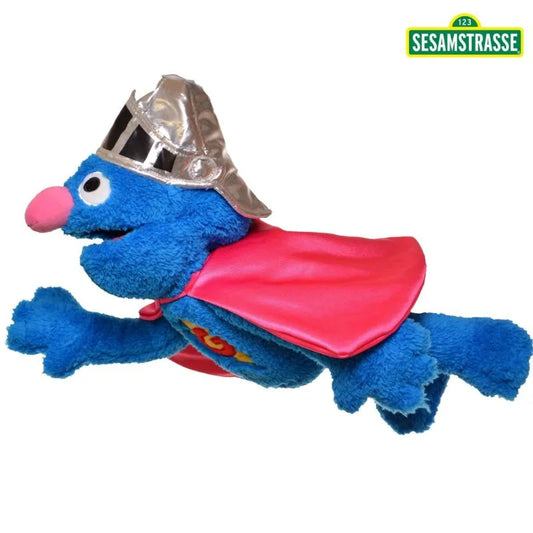 The Living Puppets Super Grover Hand Puppet features a blue puppet dressed in a silver helmet and red cape, striking a flying pose against a white background. The iconic green "Sesamstrasse" logo is prominently displayed in the top right corner, adding an authentic Sesame Street element.