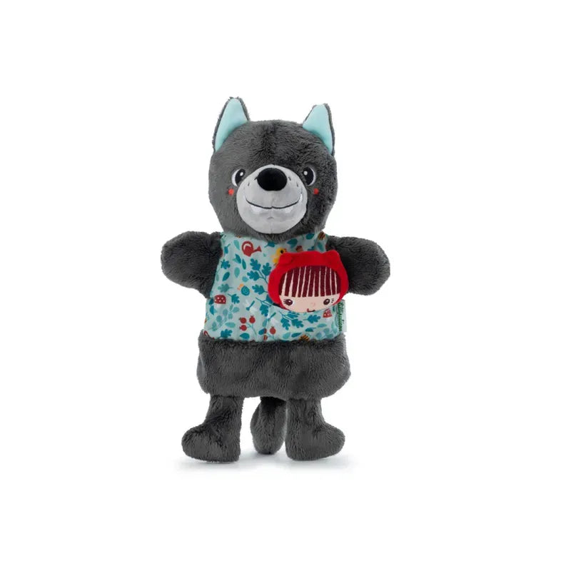 A Lilliputiens Louis Wolf Handpuppet, featuring a friendly expression with blue inner ears. It wears a colorful patterned shirt showcasing a small illustration of Little Red Riding Hood on the front, perfect for imaginative and creative play. The toy stands upright with its arms slightly outstretched.