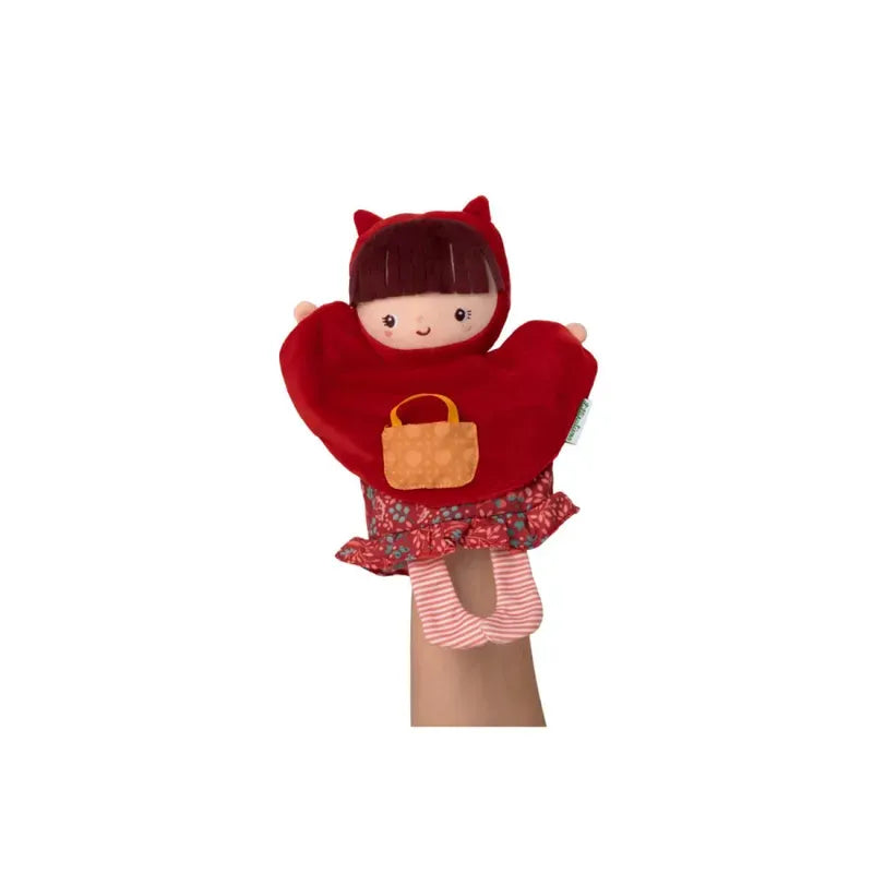 Hand holding a Lilliputiens Red Riding Hood Handpuppet of a child-like character with brown hair, wearing a red hood and cape, a red-patterned skirt, striped leggings, and carrying a small orange bag. The puppet has a friendly, smiling face—perfect for imaginative and creative play with young children.