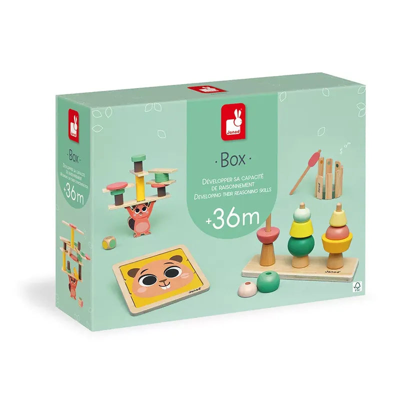 A Janod Box of Toys 36 Months for children aged 36 months and older. The set includes colorful stacking rings, a wooden balancing monkey board, and a pattern board with shaped pieces. The packaging highlights the toys' ability to develop reasoning skills.