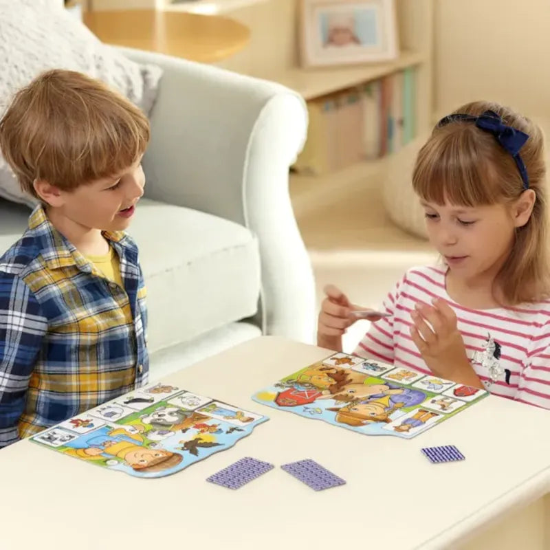 Two children, a boy and a girl, are sitting at a table playing *Orchard Toys Old Macdonald Lotto*, a colorful board game. The boy is wearing a plaid shirt and laughing, while the girl, in a striped shirt, focuses intently on the game. The room is cozy with a white couch and bookshelf in the background.