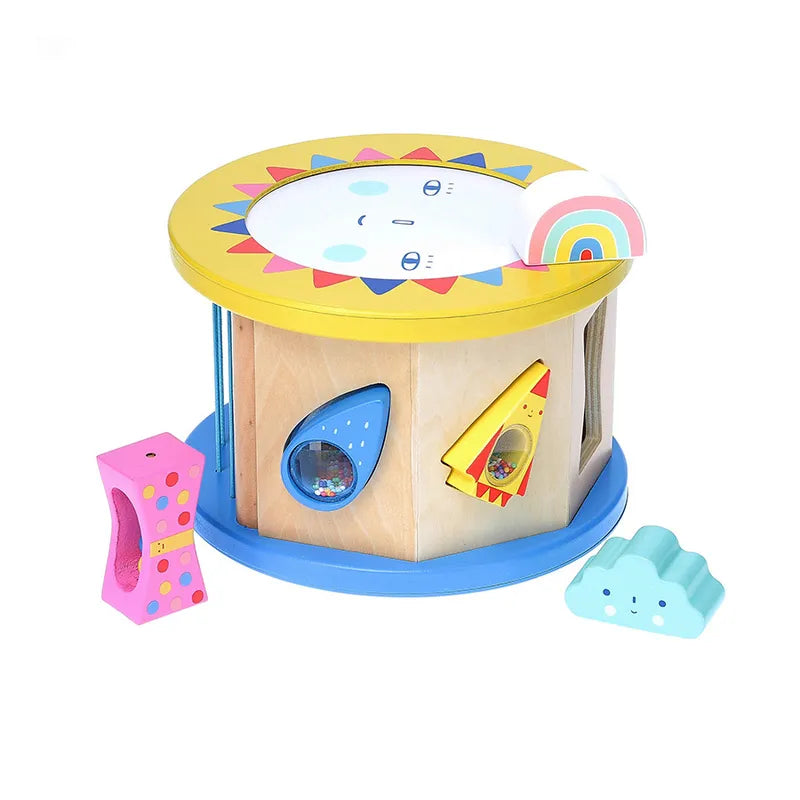 The Vilac Night and Day Shape Sorter is a vibrant wooden toy cylinder adorned with a cheerful sun face on top. It includes various cutouts in the shapes of stars, rainbows, and clouds. Designed to foster early learning, this toy aids in developing fine motor skills as children match and insert three colorful shapes (pink, yellow, blue) into the sorter.