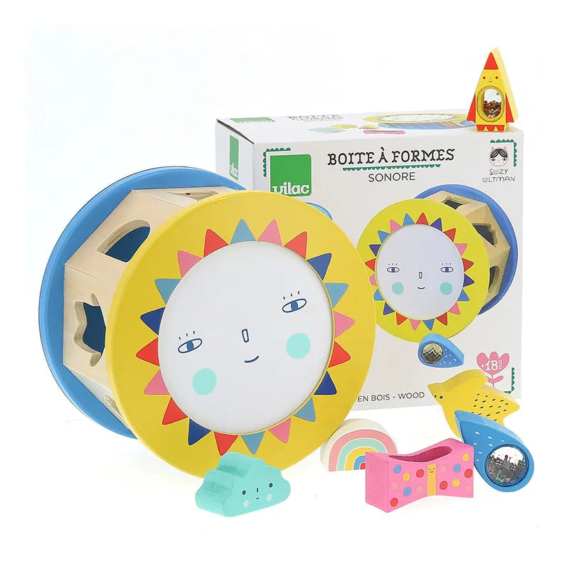 Image of the Vilac Night and Day Shape Sorter, a colorful wooden toy depicting a sunshine face with assorted shapes around it. The original packaging box is in the background, illustrating the same sunshine face and shapes. Ideal for ages 18 months and up, this toy promotes early learning and fine motor skills development.